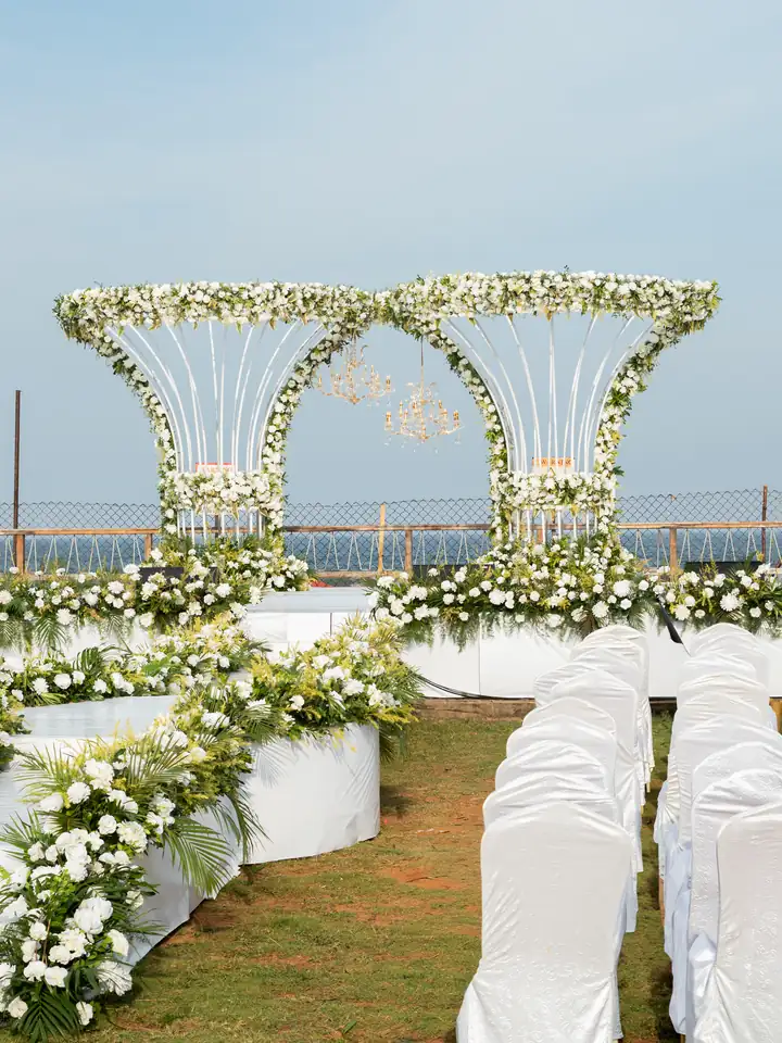 View down a white floral aisle to twin flower arches on a wedding stage by the sea