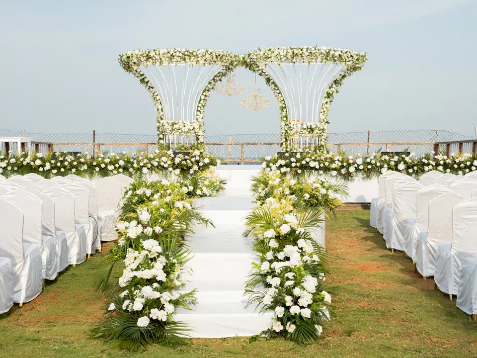 White carpeted aisle and steps lined with white flowers and palm leaves, leading up to the ceremony stage