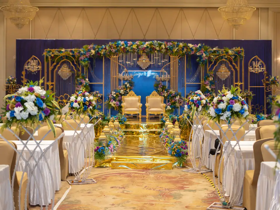 Gold aisle lined with floral stands leading to the lit blue and gold reception stage