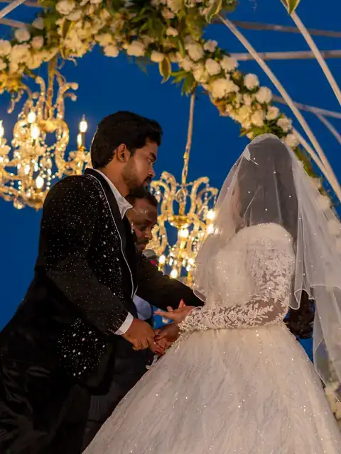 Couple beneath a floral arch hung with crystal chandeliers at night