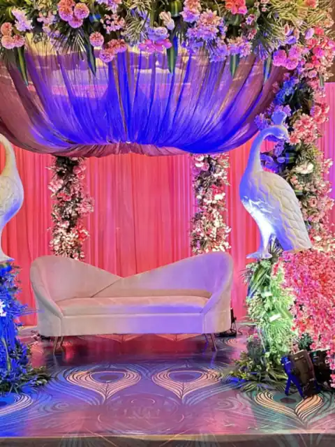 Peacock themed stage with pink florals and blue lighting