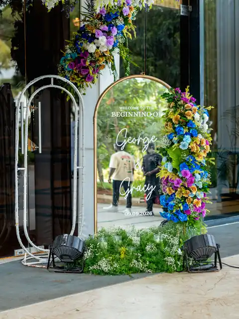 Mirror welcome sign framed by a white arch and cascading blue, purple and yellow flowers